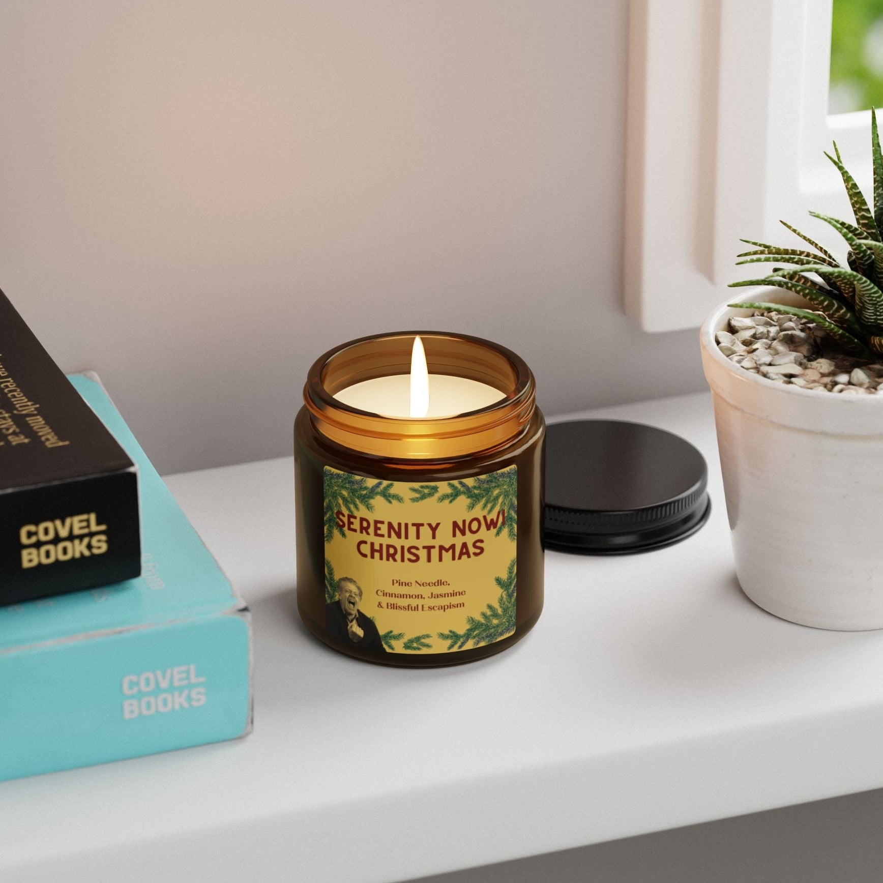 Candle labeled 'Serenity Now Christmas' on a shelf with books and a plant 4oz
