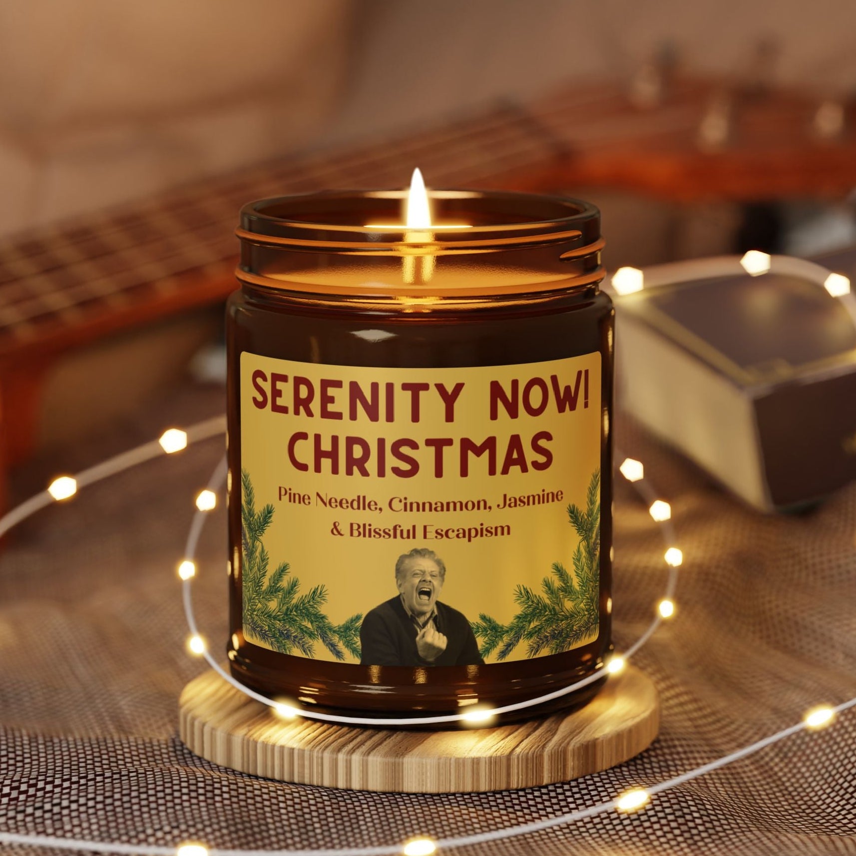 Candle in a jar labeled 'Serenity Now Christmas' with decorative lights and guitar in the background 9oz