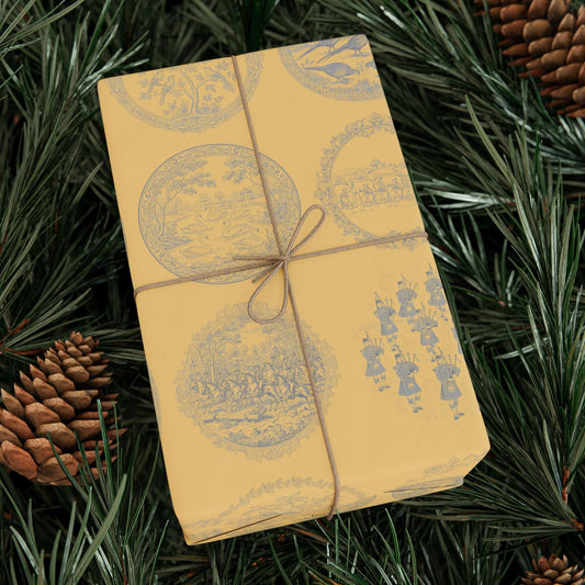 Gift box wrapped in yellow paper with decorative patterns and tied with string, surrounded by pine branches and cones.